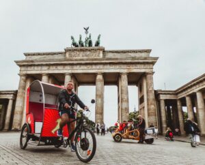 Rickshaw riders in front of the iconic Brandenburg Gate in Berlin, a popular tourist attraction.